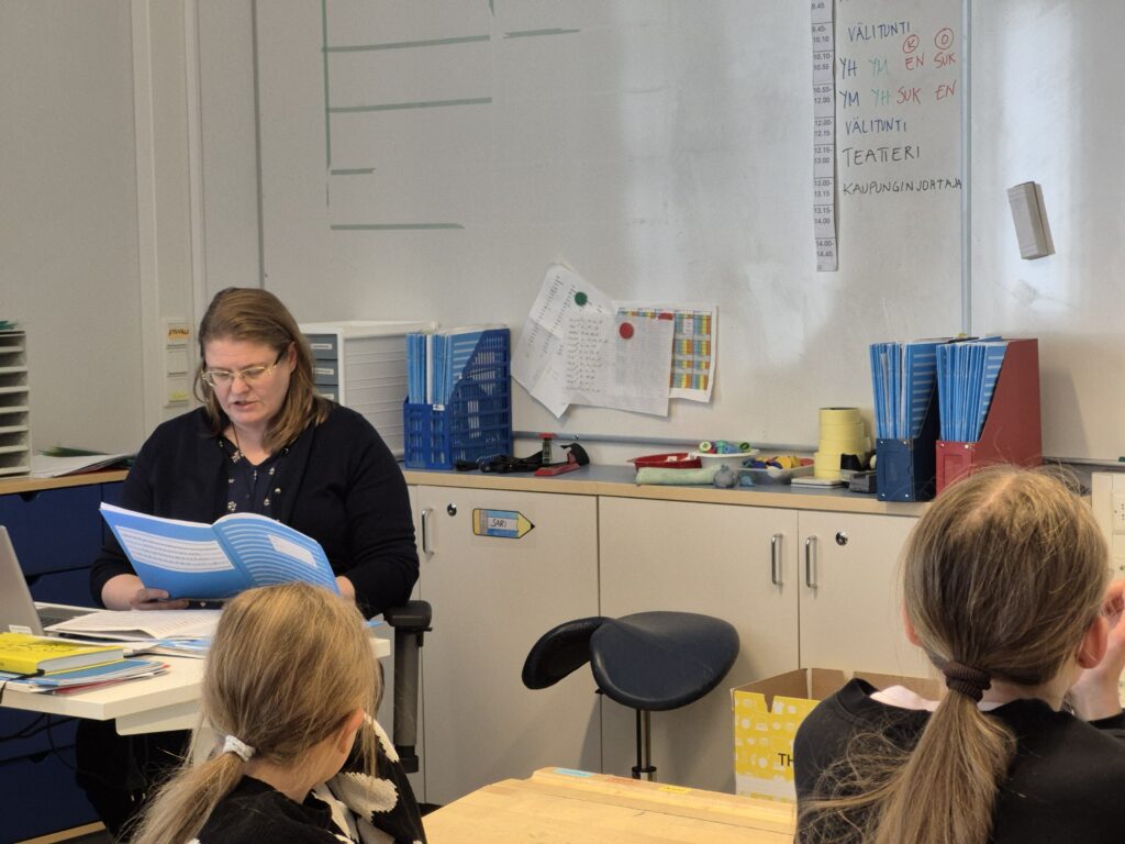 Opettaja lukee tarinaa sinisestä vihkosta. Oppilaat kuuntelevat.