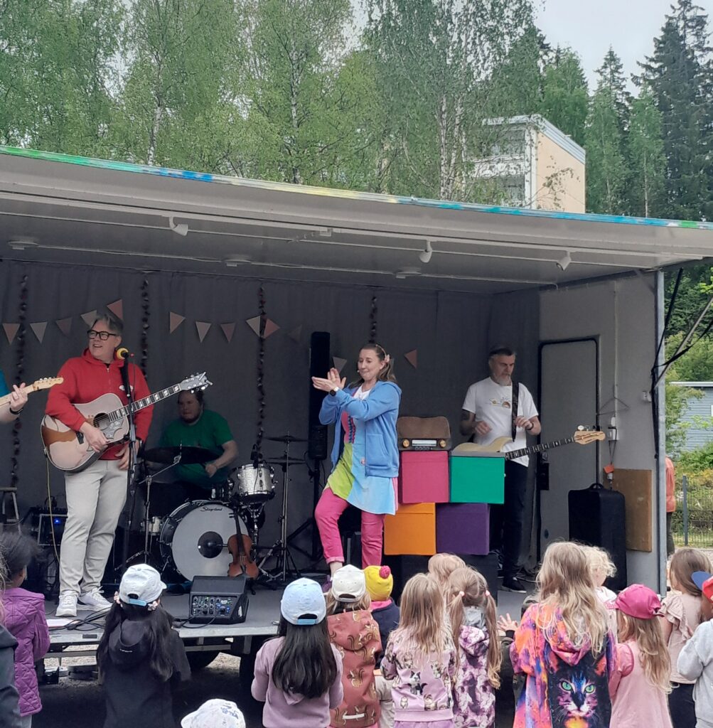Nainen ja mies esittää musiikkia lavalla. Lapsia kuuntelemassa.