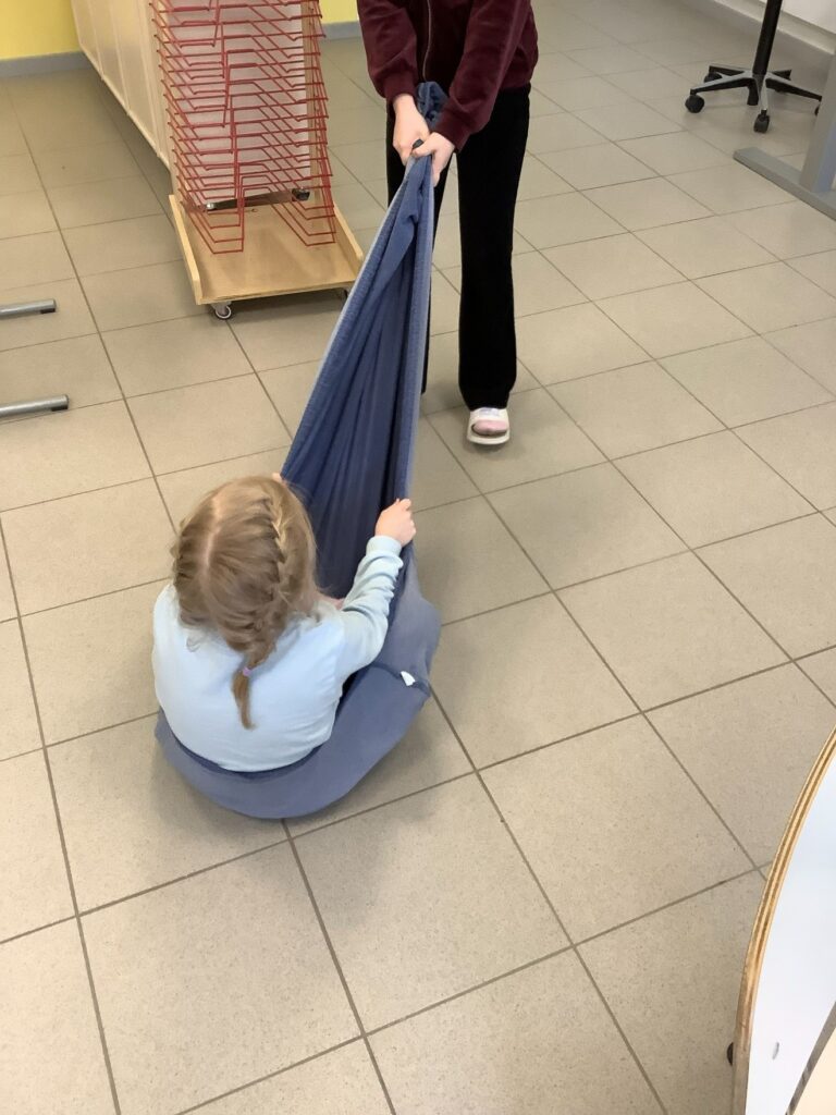 Toinen lapsi vetää peittoon kietoutunutta lasta lattiaa pitkin.