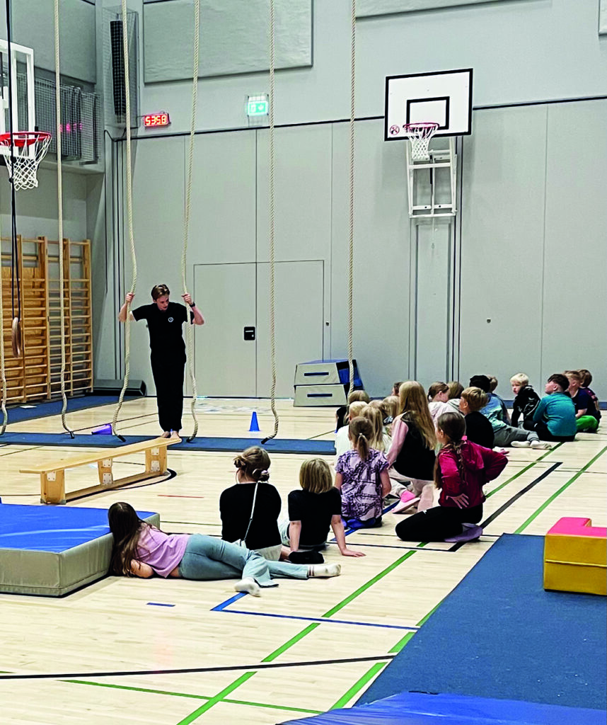 Lapsia liikuntasalissa kuuntelemassa ohjaajaa.