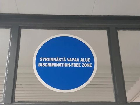 Suuri pyöreä tarra ikkunassa, jossa lukee "Syrjinnästä vapaa alue, Disrimination-Free Zone".