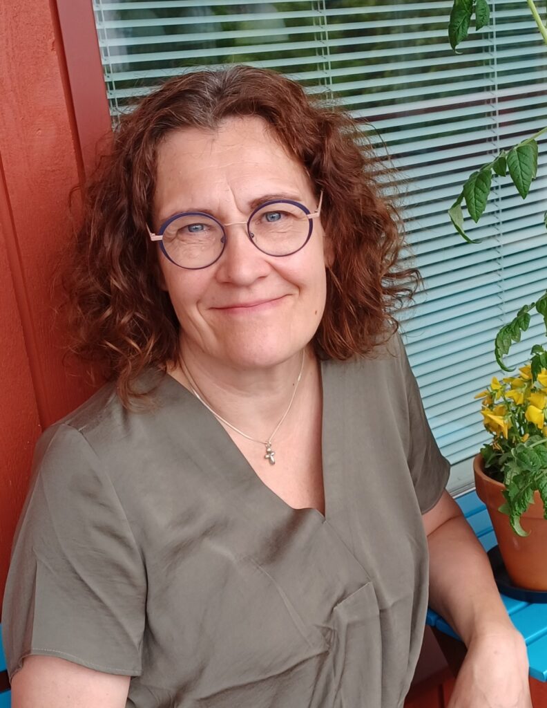 Tummatukkainen, silmälasipäinen nainen hymyilee kuvassa.