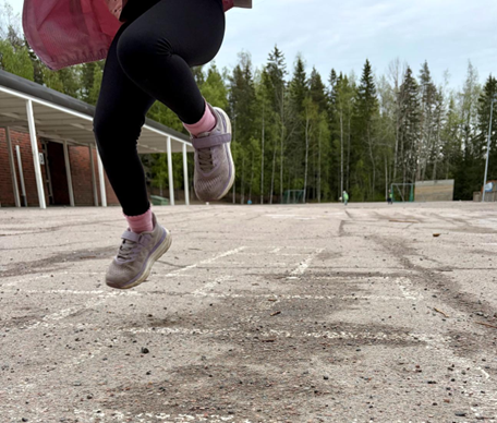 Lapsi hyppelee koulun hiekkakentällä. Kuvassa näkyy lapsen jalat.