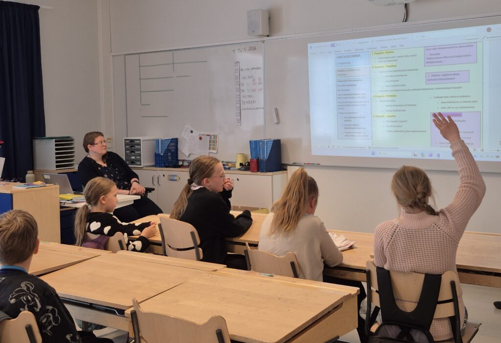 Opettaja ja oppilaat katsovat valotaulua. Yksi oppilas viittaa.