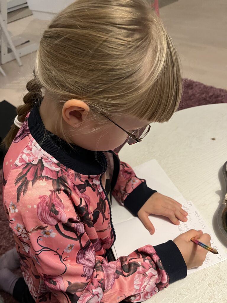 Silmälasipäinen tyttö kirjoittaa kynällä vihkoon.