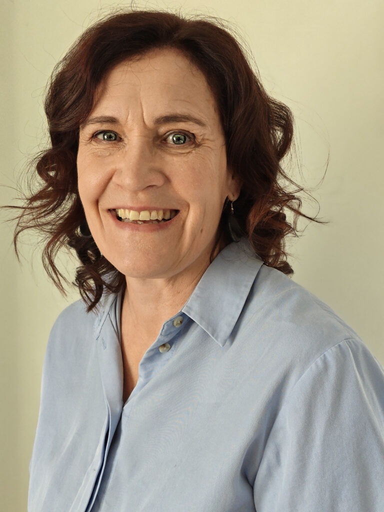 Tummahiuksinen nainen hymyilee kuvassa. Hänellä on päällään vaaleansininen paitapusero.