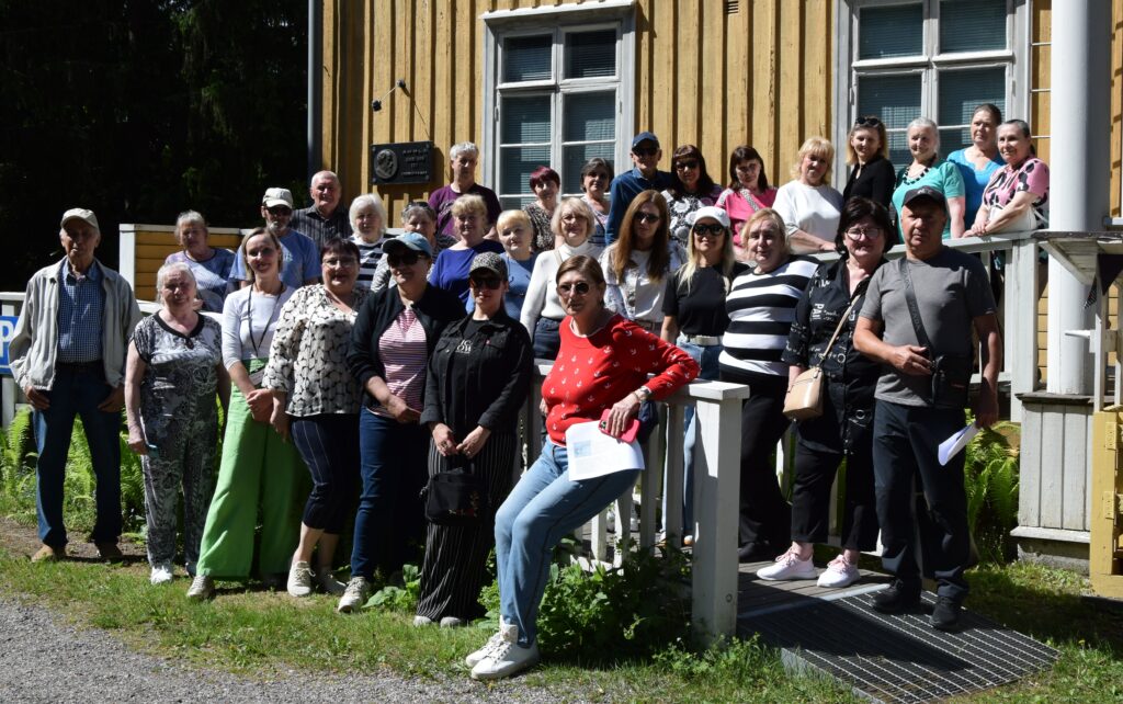 Joukko ihmisiä keltaisen puutalon edustalla.