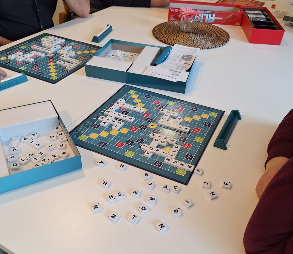 Osallistujat pelaamassa sanapeliä. Pöydällä Scrabble-sanapeli sekä Alias-sananselityspeli.