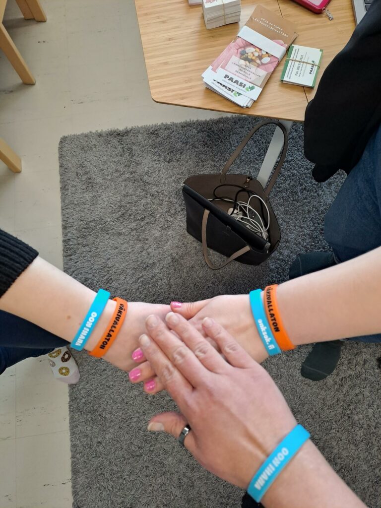 Lähikuva kolmesta kämmenpöydästä, kaikissa rannekoru, joissa lukee "Väkivallaton".