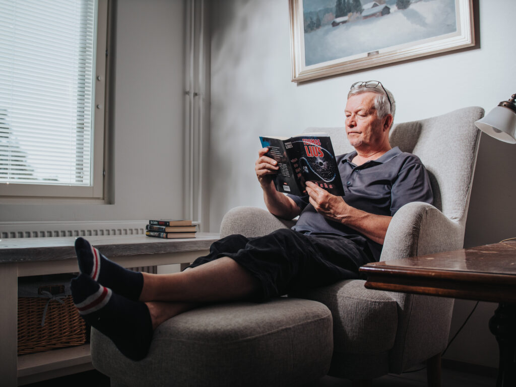 Ari Honkanen istuu nojatuolissa lukemassa kirjaa.