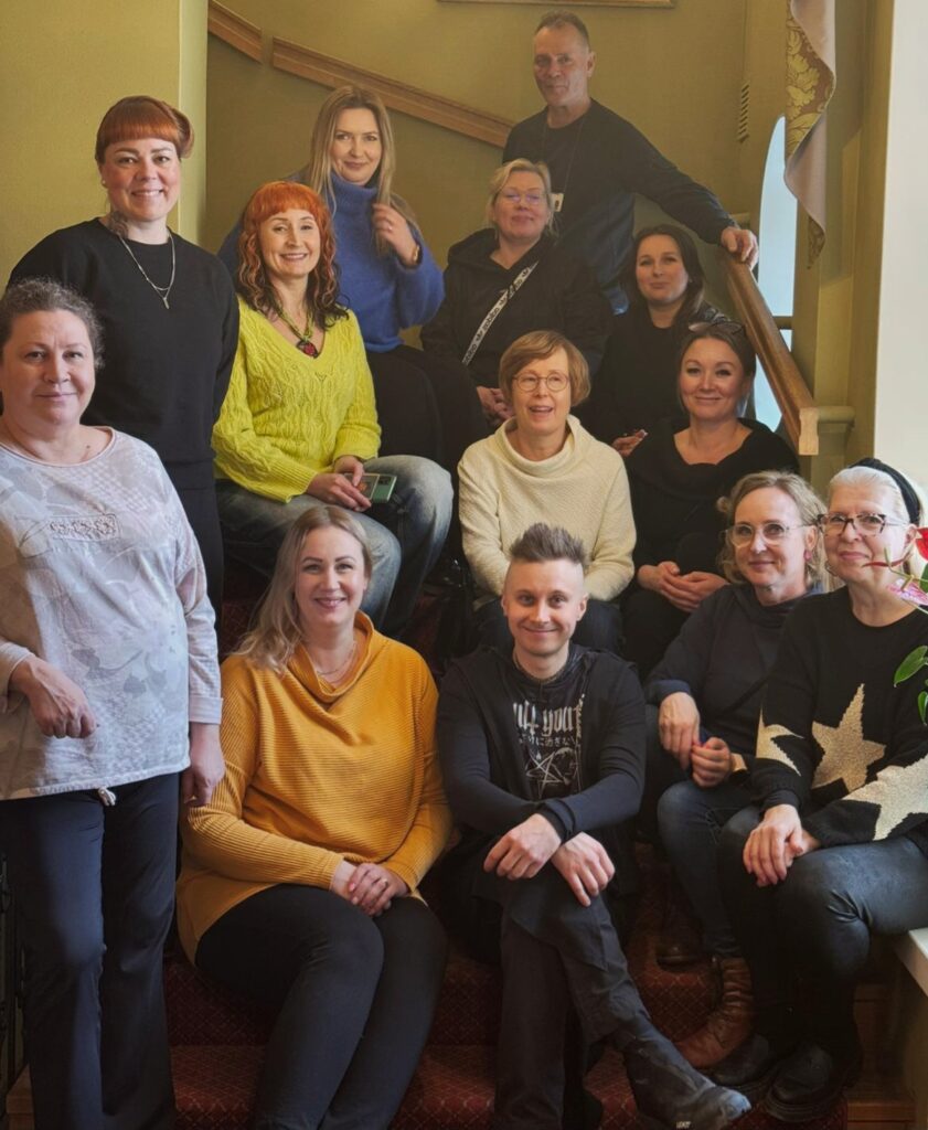 Ihmisiä ryhmäkuvassa portaikkokäytävässä. He hymyilevät.