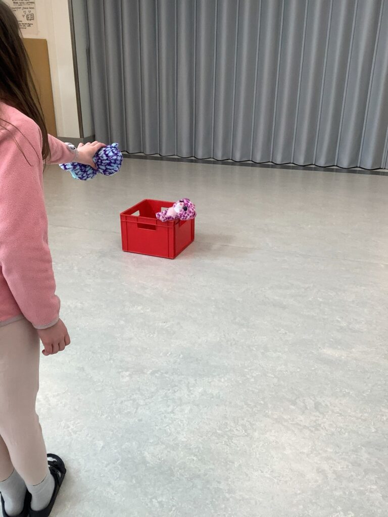 Lapsi heittää pehmoleluja lattialla olevaan koriin.
