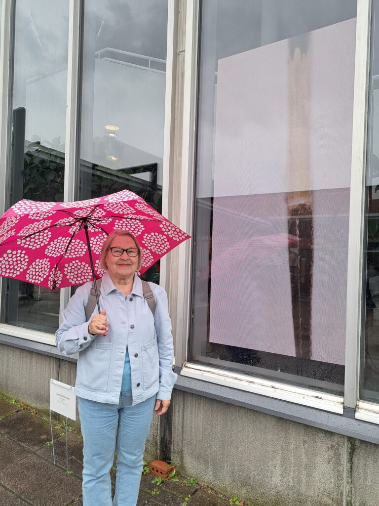 Nainen seisoo sateenvarjo kädessä mediataideteoksen vierellä.