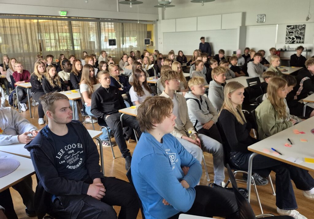 Joukko nuoria istumassa isossa salissa ja kuuntelemassa esitystä.