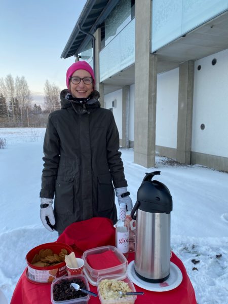 Henkilö seisoo ulkona talvisessa maisemassa, edessään pöydällä iso termostaatti ja pipareita.