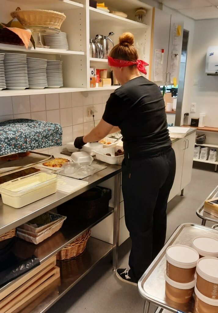 Keittiötyöntekijä pakkaamassa ruokaa laatikkoon keittiötiloissa.