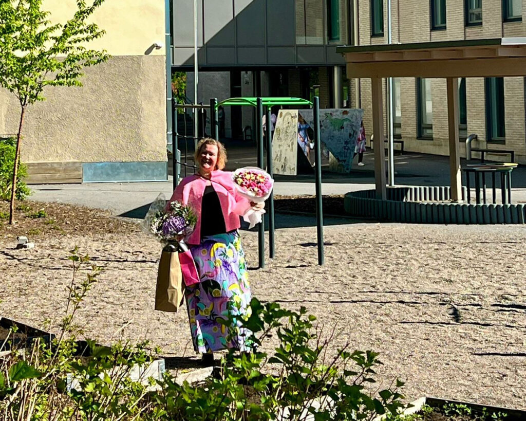 Jenni Hietanoro Harjulan koulun edessä kukkakimppuja ja lahjoja käsissään.