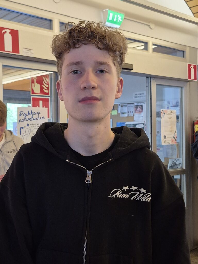 Kiharahiuksinen poika lähikuvassa. Hänellä on päällään musta huppari.