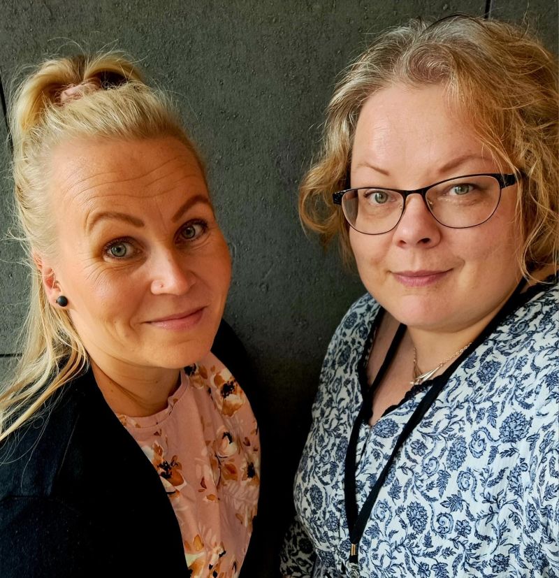 Kaksi vaaleahiuksista naista hymyilee kuvassa. Toisella henkilöllä on silmälasit päässä.