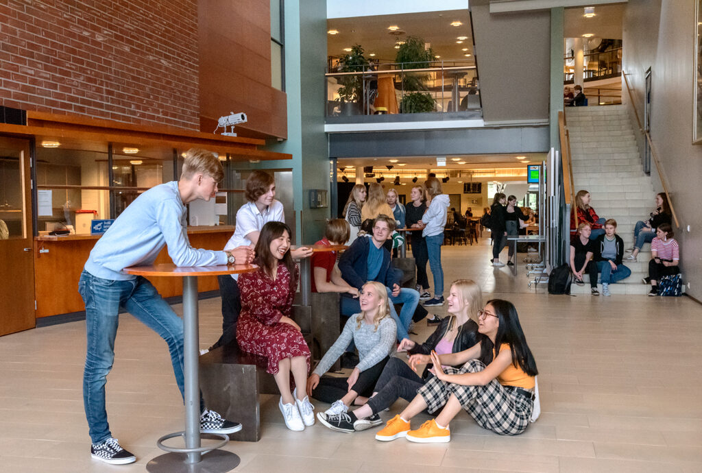 Opiskelijoita istumassa ja hymyilemässä toisilleen rakennuksen aulassa.