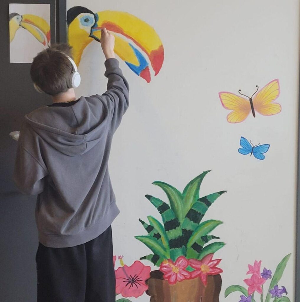 Oppilas maalamassa seinälle isoa värikästä tukaania.